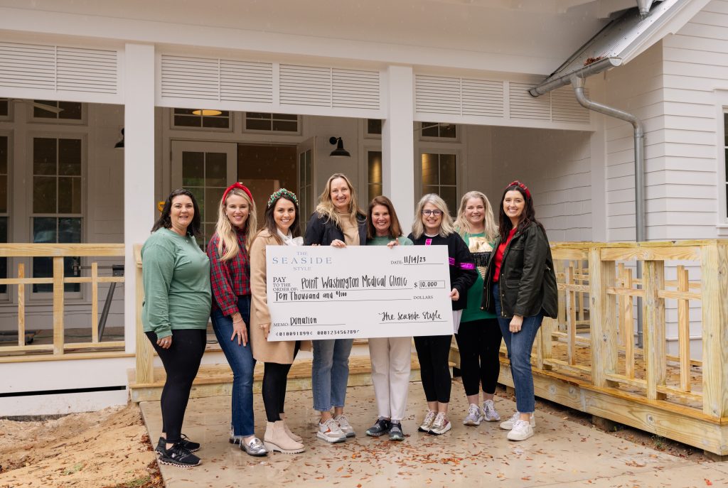Group of women standing outside a building, smiling and holding a large donation check for a local medical clinic