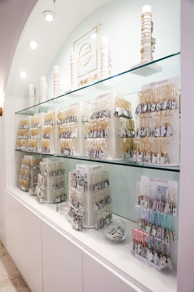 Wall display of neatly arranged gold and silver bracelets and jewelry on clear stands inside a bright boutique.