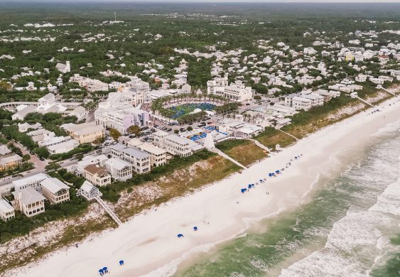 Aerial view of beachfront town with white sand beach, ocean waves, and coastal buildings.