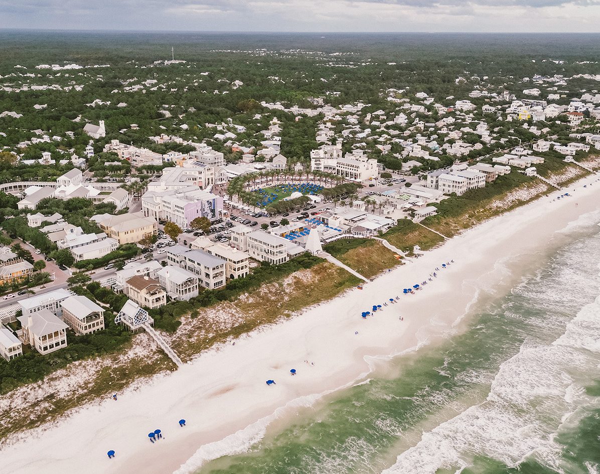 Aerial view of beachfront town with white sand beach, ocean waves, and coastal buildings.