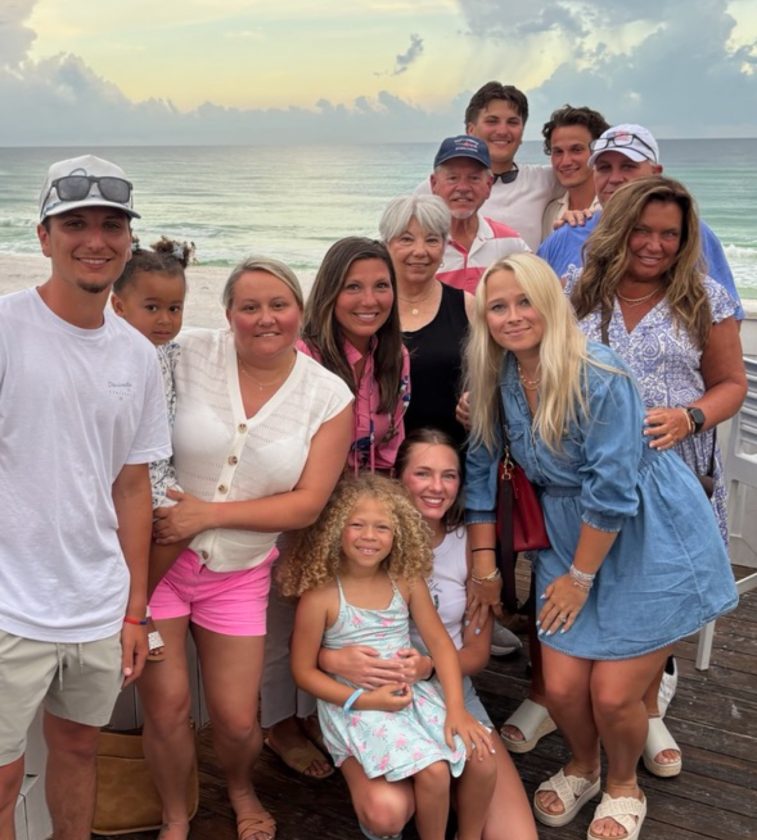 Group of family and friends posing on beachside deck at sunset with ocean backdrop.