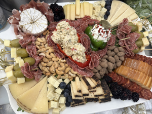 Abundant charcuterie board piled with meats, cheeses, nuts, olives, stuffed peppers, and fresh berries.