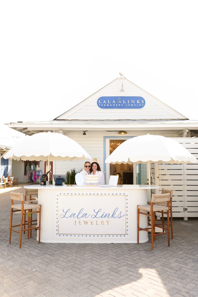 Outdoor Lala Links jewelry kiosk with white umbrellas and staff standing behind branded counter.