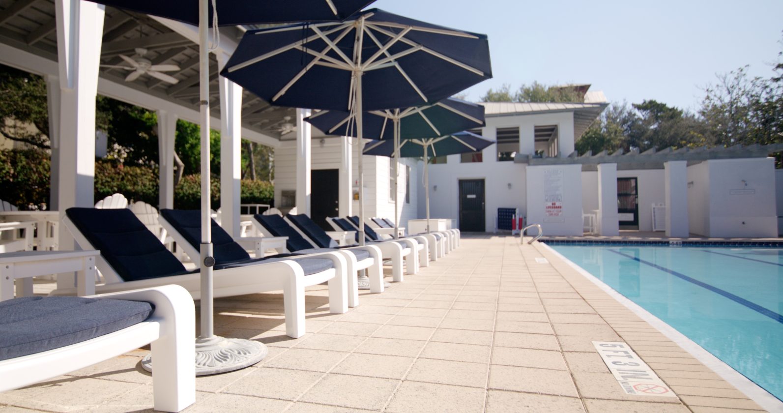 Row of navy cushioned loungers and umbrellas lining a quiet outdoor pool at modern clubhouse.
