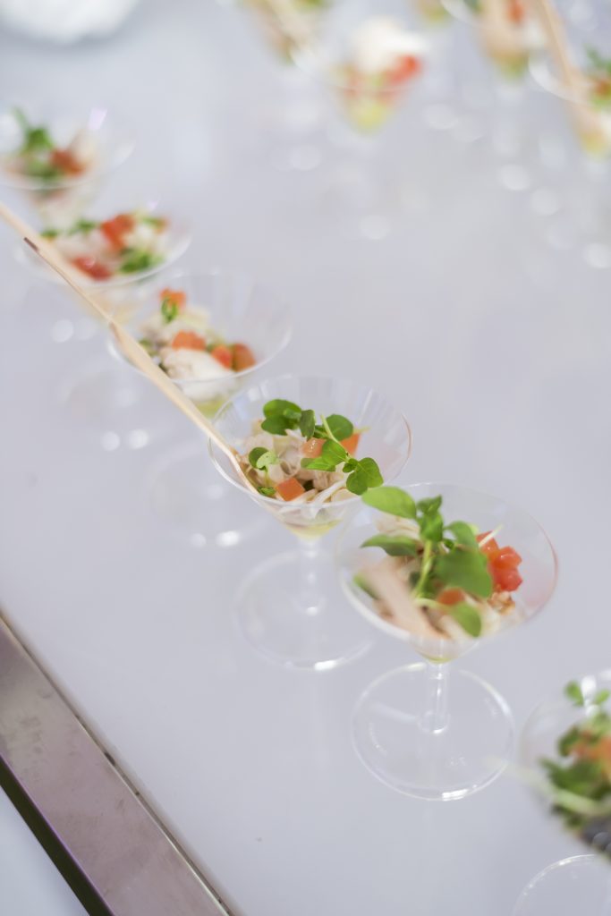 Row of mini appetizer salads in martini glasses, garnished with greens and diced vegetables.