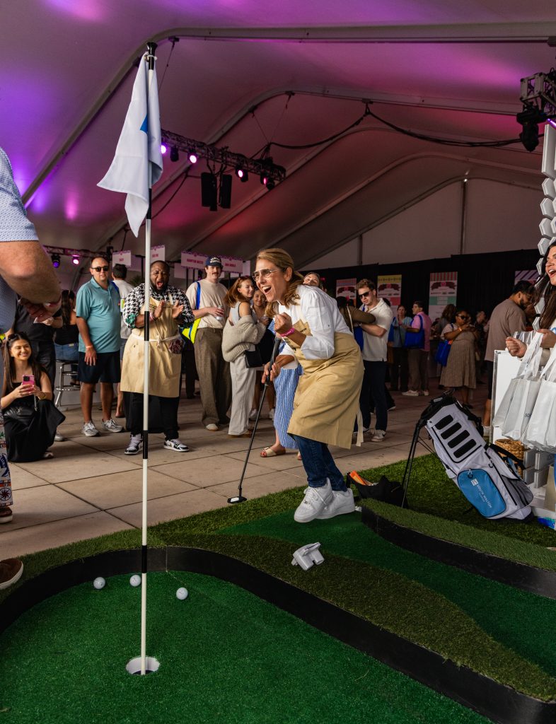 Person celebrating while putting on mini golf course inside lively event tent.