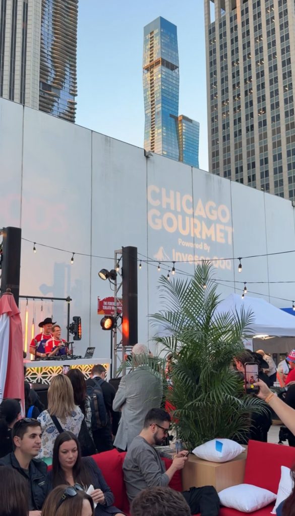 Crowded outdoor Chicago Gourmet event with live music and city skyscrapers backdrop.