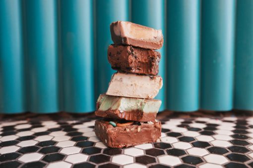 Stack of assorted chocolate fudge squares on black-and-white tile against turquoise wall.