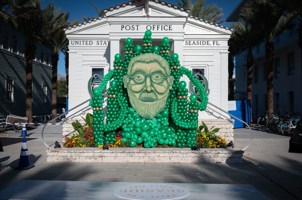 Green balloon sculpture of a bearded face displayed in front of the Seaside, Florida post office.