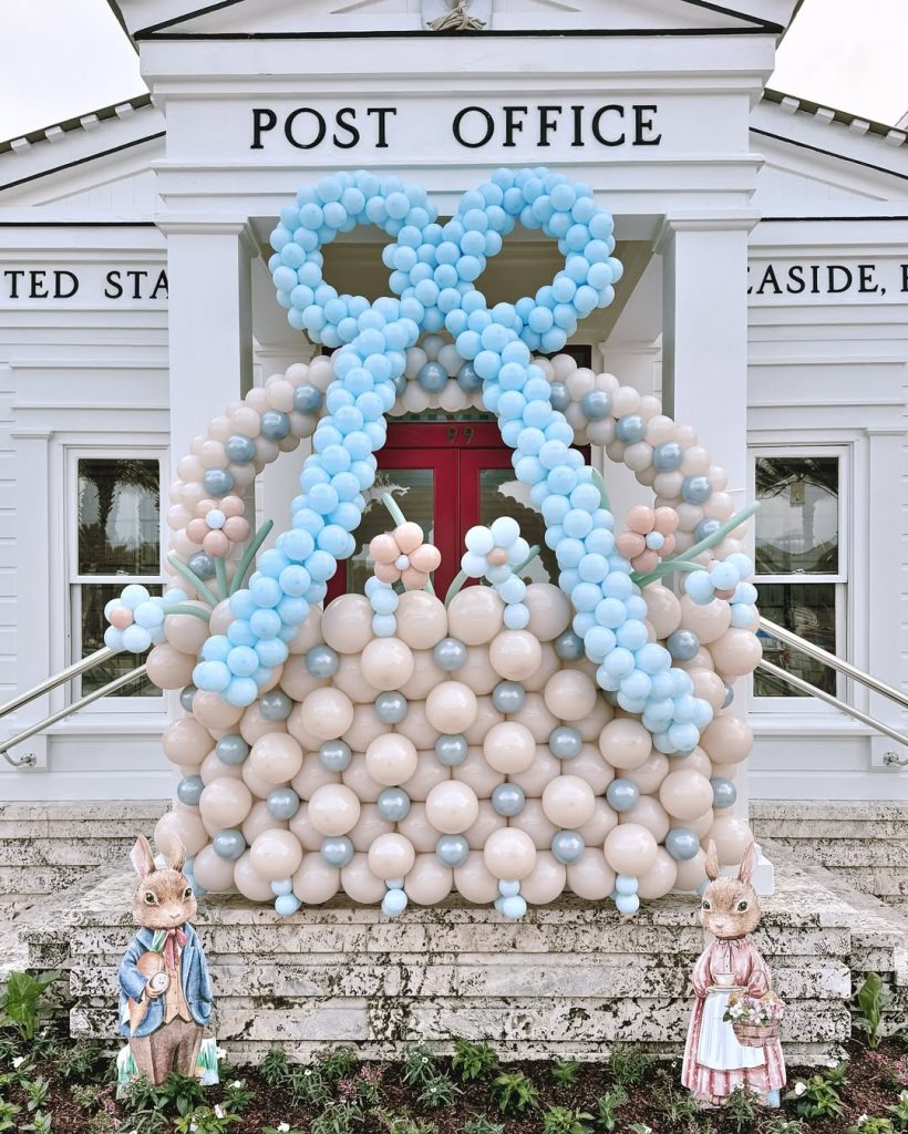 Large pastel balloon basket with bow displayed in front of a white post office, flanked by decorative Easter rabbits