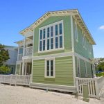 Two-story light green house with white trim and a picket fence under a clear blue sky.
