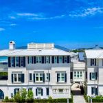 Three-story white beach house with dark blue shutters against a bright blue sky.