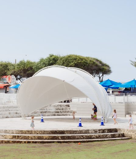 Children playing around a white canopy structure in an outdoor area with food trucks, umbrellas, and palm trees