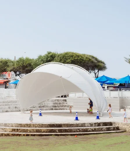 Children playing around a white canopy structure in an outdoor area with food trucks, umbrellas, and palm trees