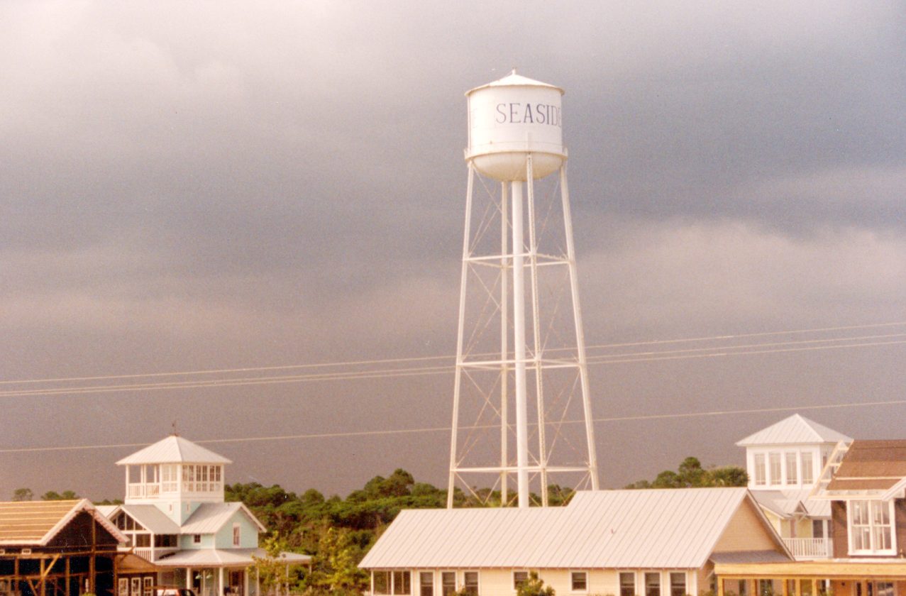 Vintage-style photo of the Seaside water tower rising above coastal homes under dark storm clouds.