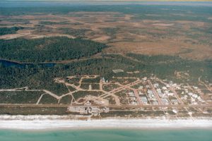 Aerial view of a coastal beachfront community with forest, wetlands, and turquoise ocean water.