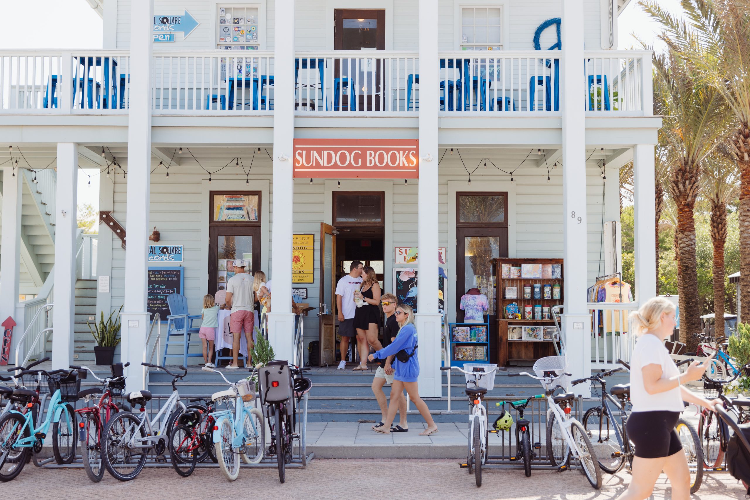 Busy beachfront bookstore with parked bicycles, shoppers, and a white porch-front building on a sunny day.