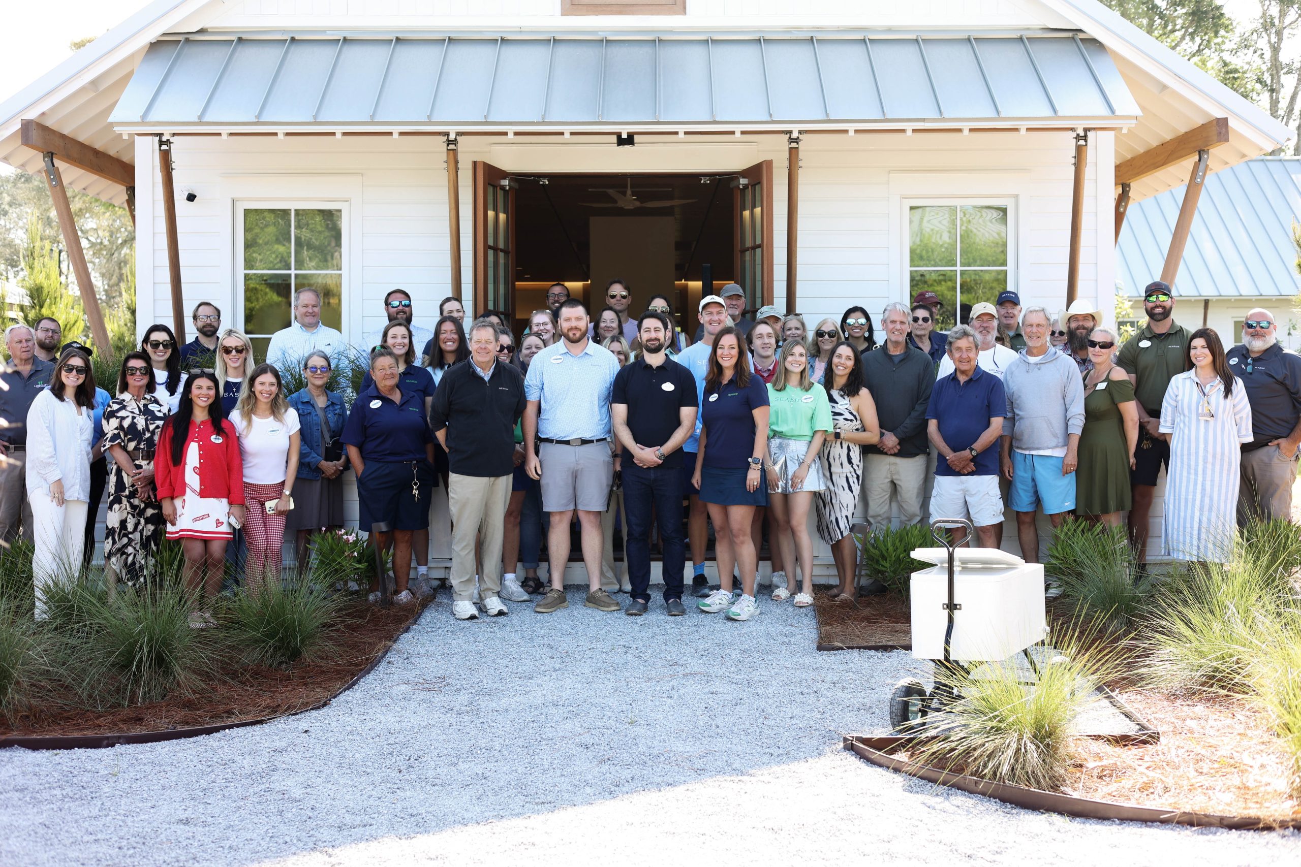 Group photo of a large team standing outside a white building with a metal roof.