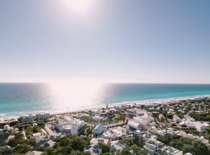 45 facts about seaside florida 30a Aerial view of Seaside, Florida's white coastal town nestled among trees along the turquoise Gulf of Mexico under a bright, sunlit sky.