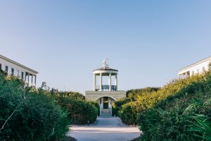 45 facts about seaside florida 30a One of Seaside's iconic white beach pavilions viewed down a tree-lined pedestrian path, with dune vegetation and coastal architecture on either side.